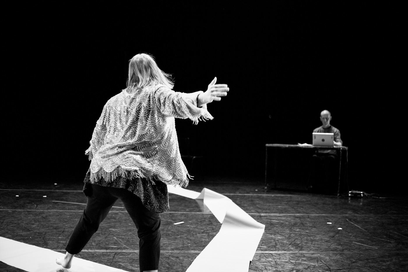 Black and white photo of a woman dancing with her back towards the camera traveling to a man sitting at a desk